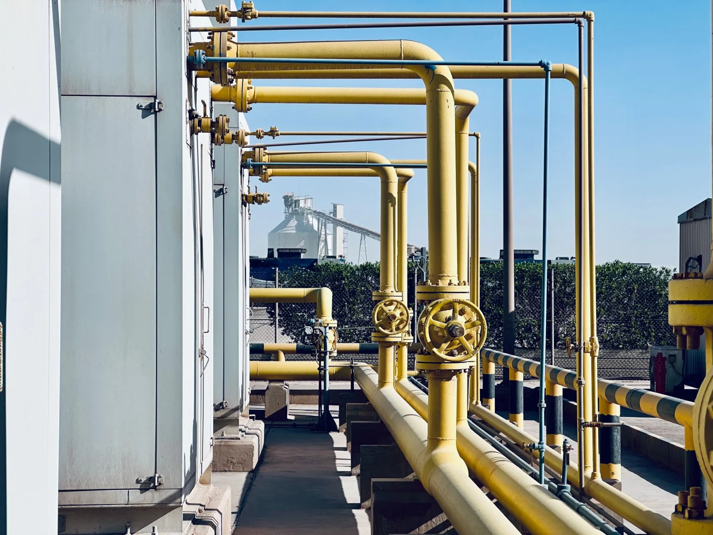 Yellow industrial gas pipework and valves beneath a blue sky